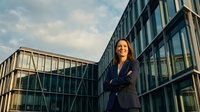 Confident businesswoman with crossed arms standing in front of modern office building during golden hour sunset creating professional corporate atmosphere.