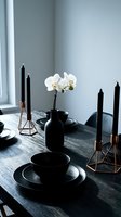 Elegant black dinnerware set with copper candlesticks and white orchid on dark wooden table creating sophisticated dining atmosphere for entertaining.