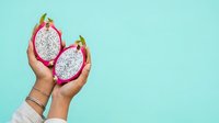 Female hands holding two halves of fresh dragon fruit with white flesh against turquoise background, suitable for food, nutrition, and healthy lifestyle content.