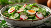 Fresh spring salad with sliced radishes, soft boiled eggs, cucumber, and herbs in ceramic bowl garnished with dill and parsley. Healthy seasonal dish.