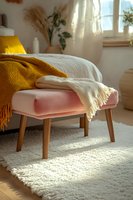 Cozy pink ottoman with wooden legs draped in white and mustard yellow knit throws, sunlit room with plush carpet and natural decor, warm morning light.