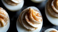 Deviled eggs topped with paprika and garnish, arranged on dark surface. Appetizer for parties, gatherings, catering, restaurants, food blogs, cookbooks, menus.