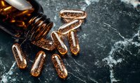 Glowing golden capsules with sparkles spilled from brown glass bottle on dark marble background. Medical supplements and vitamins concept.