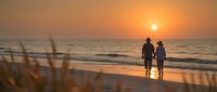 Romantic couple walking hand in hand on beach at sunset with golden sky and ocean waves, silhouetted against warm evening light for travel and love concepts.