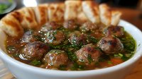 Homemade meatball soup with fresh herbs, carrots and savory broth served in white ceramic bowl, garnished with parsley and accompanied by crusty bread.