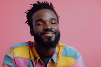 Happy young African American man with dreadlocks wearing colorful striped shirt smiling broadly against pink background. Portrait for lifestyle content.
