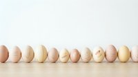 Row of natural organic eggs in various shades from brown to cream arranged on wooden surface against white background for cooking and nutrition concepts.