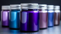 Colorful metallic jars with silver screw caps arranged in row, purple and blue glass containers on dark surface with selective focus on front bottle.