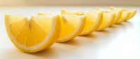 Fresh lemon slices arranged in a neat row on a white surface, showcasing vibrant yellow citrus wedges with juicy texture.