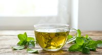 Fresh mint herbal tea in transparent glass cup on wooden table with green leaves, natural wellness drink for relaxation and health benefits.