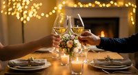 Romantic dinner celebration with couple toasting white wine glasses by fireplace with warm bokeh lights creating intimate dining atmosphere for anniversary.