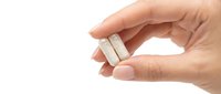 Hand holding small white USB flash drive between fingers on clean white background isolated for technology and data storage concepts.