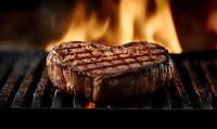 Juicy grilled beef steak with grill marks cooking over flaming fire. Close up of meat on barbecue grate with flames in background. Culinary and food photography.