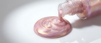 Pouring shimmering pink liquid slime from bottle onto white surface, creating swirled puddle effect for sensory play, craft projects, and creative content.