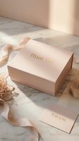 Elegant blush pink gift box with gold Thank You lettering on marble surface with satin ribbon and With Love card for luxury gifting.