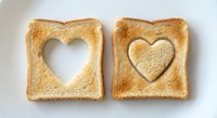 Golden toasted bread slices with heart-shaped cutouts on white background, perfect for breakfast, love-themed food photography and romantic dining concepts.