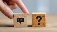 Wooden blocks with communication symbols - speech bubble and question mark on wooden table, representing customer service, FAQ, or business communication concept.
