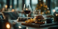 Gourmet burger with sesame bun and golden fries served on wooden board with red wine glass in elegant restaurant setting with warm ambient lighting.