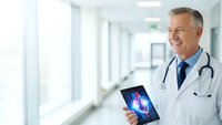 Smiling mature Caucasian male doctor in white coat with stethoscope holding digital tablet showing spine X-ray in modern hospital corridor for medical consultation.