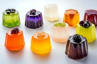 Colorful fruit jelly desserts with berries and mint garnish arranged on white surface, showcasing variety of flavors for catering or party menu.
