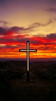 Wooden cross silhouetted against dramatic sunset sky with vibrant orange and red clouds over desert landscape for spiritual and religious themes.