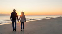 Senior couple walking hand in hand on beach at sunset, romantic golden hour moment by ocean waves, retirement lifestyle and love concept.