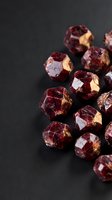 Deep red garnet gemstones with faceted cuts scattered on dark background for jewelry design and luxury accessories.