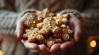 Hands holding freshly baked gingerbread cookies with white icing decorations, including snowflakes and gingerbread man shapes in warm holiday setting.
