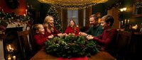 Multi-generational Caucasian family gathered around dining table with evergreen centerpiece during Christmas celebration in cozy home interior with fireplace.