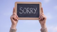 Hands holding small chalkboard with sorry message written in white chalk against soft purple background for apology communication concepts.