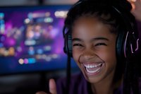 Young African American female gamer wearing headphones smiles brightly while streaming or playing video games, with purple LED lighting and bokeh effects in background.
