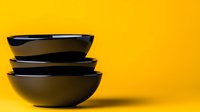 Stack of black ceramic bowls on vibrant yellow background, minimalist kitchen tableware arrangement for food photography and modern dining presentation.
