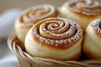 Fresh baked cinnamon rolls with powdered sugar dusting in woven basket, close up view showing soft dough texture and spiral pattern of sweet filling.