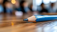Blue sharpened pencil lying on wooden desk surface with blurred office background and warm lighting for creative workspace concepts.