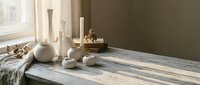 Minimalist bathroom vanity with ceramic vessels, candles, and natural decor on weathered wood surface near window with soft natural light.