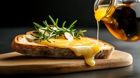Fresh bread slice with melted cheese, drizzled honey and aromatic rosemary sprig on wooden cutting board against dark background. Food photography for menu design.