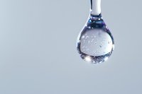 Crystal clear water droplet with air bubbles suspended from a faucet against minimal gray background, showcasing purity and hydration concept.
