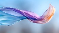 Flowing translucent fabric in gradient colors from blue to purple to pink creates elegant wave motion against soft blurred background for luxury design projects.