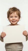 Happy toddler boy with blonde hair holding blank white paper sign for customizable message on neutral background.