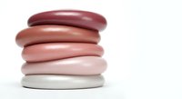 Stack of smooth oval stones in gradient pink to burgundy tones on white background, zen meditation balance concept for spa wellness and mindfulness practices.