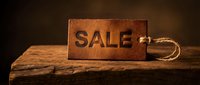 Rustic leather sale tag with embossed text resting on aged wooden surface, warm dark background evoking vintage retail and discount promotion concepts.