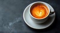Fresh latte art in white ceramic cup on dark background, heart pattern visible in golden crema, moody coffee shop atmosphere for cafe and restaurant use.