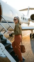 Stylish blonde businesswoman in sunglasses boarding private jet with leather handbag during golden hour for luxury travel and corporate aviation.