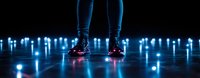Legs in dark sneakers standing on reflective surface surrounded by glowing blue LED lights creating atmospheric panoramic nightclub scene.