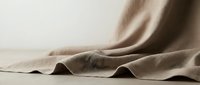 Natural beige linen fabric with soft folds and wrinkles creating elegant textile background for fashion, interior design and crafting projects.