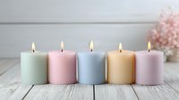 Five pastel colored candles burning with warm flames arranged on rustic white wooden surface creating peaceful spa atmosphere for relaxation and wellness.