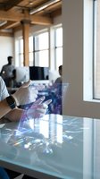 Person wearing white gloves holding transparent digital tablet with holographic interface displaying data visualization and network connections in modern office workspace with colleagues in background.