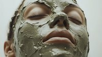 Young woman with clay facial mask during spa treatment, eyes closed in relaxation, close up view showing skincare and beauty wellness routine.