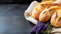 Fresh crusty baguettes on rustic linen cloth with decorative lavender sprigs, dark moody background creates dramatic food photography composition.