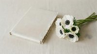 White ranunculus flowers bouquet with blank linen photo album on neutral beige background for wedding memories and special occasions photography.